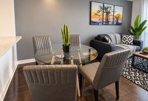 Un salon moderne avec une table à manger à plateau de verre, entourée de chaises, d’un canapé et d’une table basse.