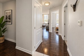 A hallway with hardwood flooring, white walls, and a framed picture on the left.