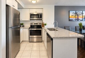 A modern kitchen with stainless steel appliances, a granite countertop, and a dining area with a view of the sunset. - Stylish 1BR+Den Retreat in Markham (Markham)