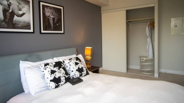 A hotel room with a bed, a nightstand, a lamp, a wardrobe, and two framed pictures on the wall. - Stylish 1BR+Den Retreat in Markham (Markham)