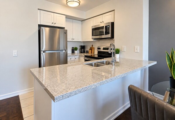 A modern kitchen with a stainless steel refrigerator, a microwave, and a granite countertop island.