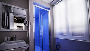 A bathroom with a white sink, a mirror, a blue shower enclosure, and a showerhead.