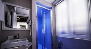 A bathroom with a white sink, a mirror, a blue shower enclosure, and a showerhead.