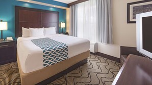 A hotel room with a large bed, a headboard, two bedside tables with lamps, a window with curtains, and a television. - La Quinta Inn Suites Central Point Medford (Central Point)