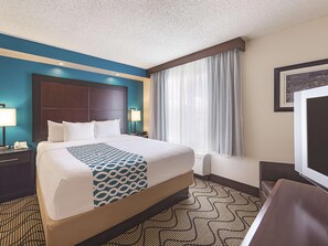 A hotel room with a large bed, a headboard, two bedside tables with lamps, a window with curtains, and a television. - La Quinta Inn Suites Central Point Medford (Central Point)