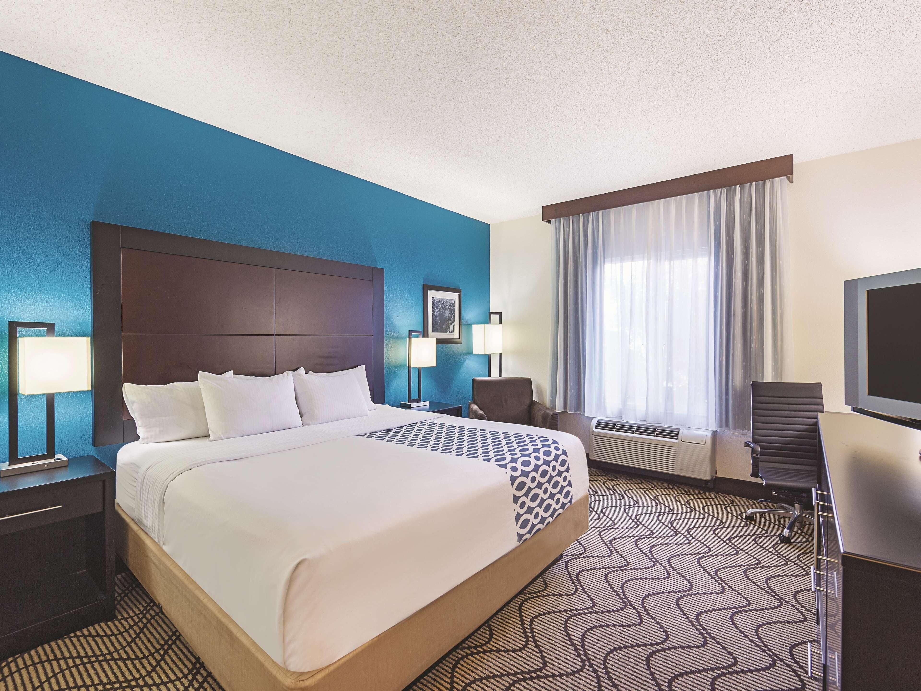 A hotel room with a large bed, a desk, a chair, a television, and a window with curtains.