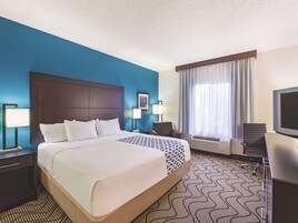 Quarto de hotel com uma cama grande, uma escrivaninha, uma cadeira, uma televisão e uma janela com cortinas.
