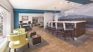 A modern hotel lobby with a bar area, seating, and a mural of a mountain. - La Quinta Inn Suites Central Point Medford (Central Point)