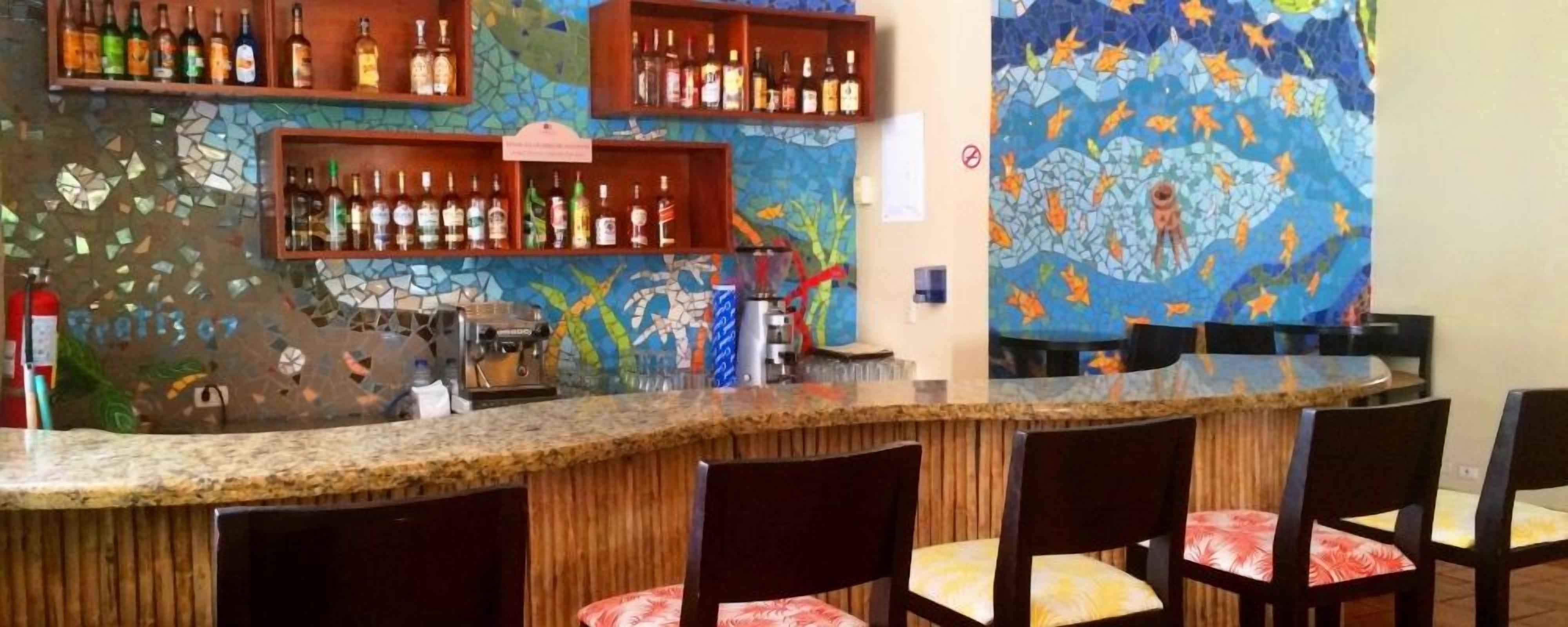 A bar area with a mosaic wall, shelves of bottles, and a coffee machine.