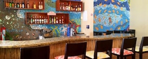 A bar area with a mosaic wall, shelves of bottles, and a coffee machine.