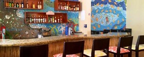 A bar area with a mosaic wall, shelves of bottles, and a coffee machine.
