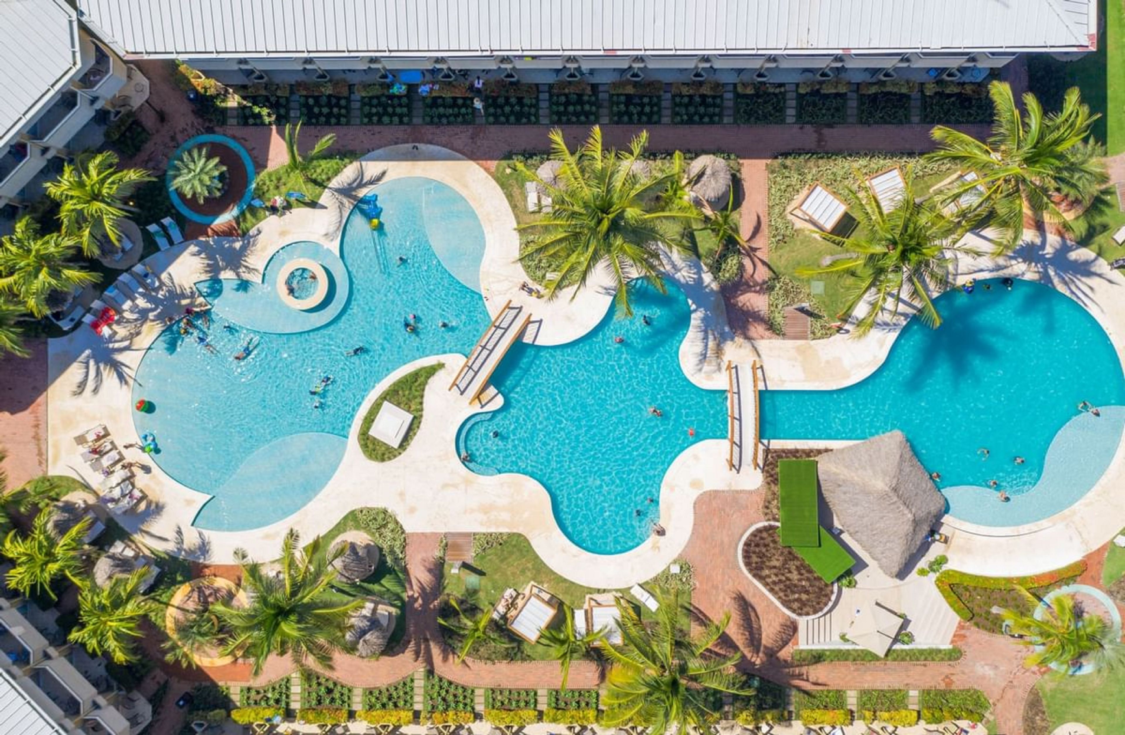 Eine Luftaufnahme eines Resorts mit mehreren Schwimmbecken, Palmen und Liegebereichen.