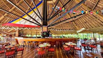 A restaurant with a high wooden ceiling, tables with red chairs, and a central bar area.