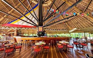 Un ristorante con soffitto in legno a volta, tavoli con sedie rosse e un'area bar centrale.