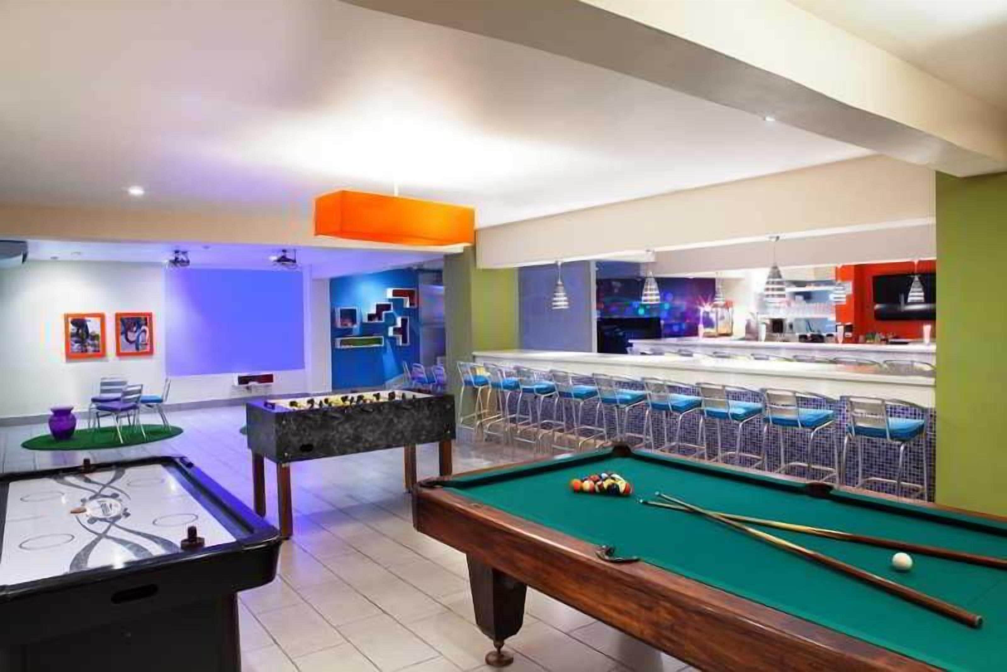 Une salle de billard équipée d’une table de billard, d’un baby-foot et d’un bar avec des tabourets.