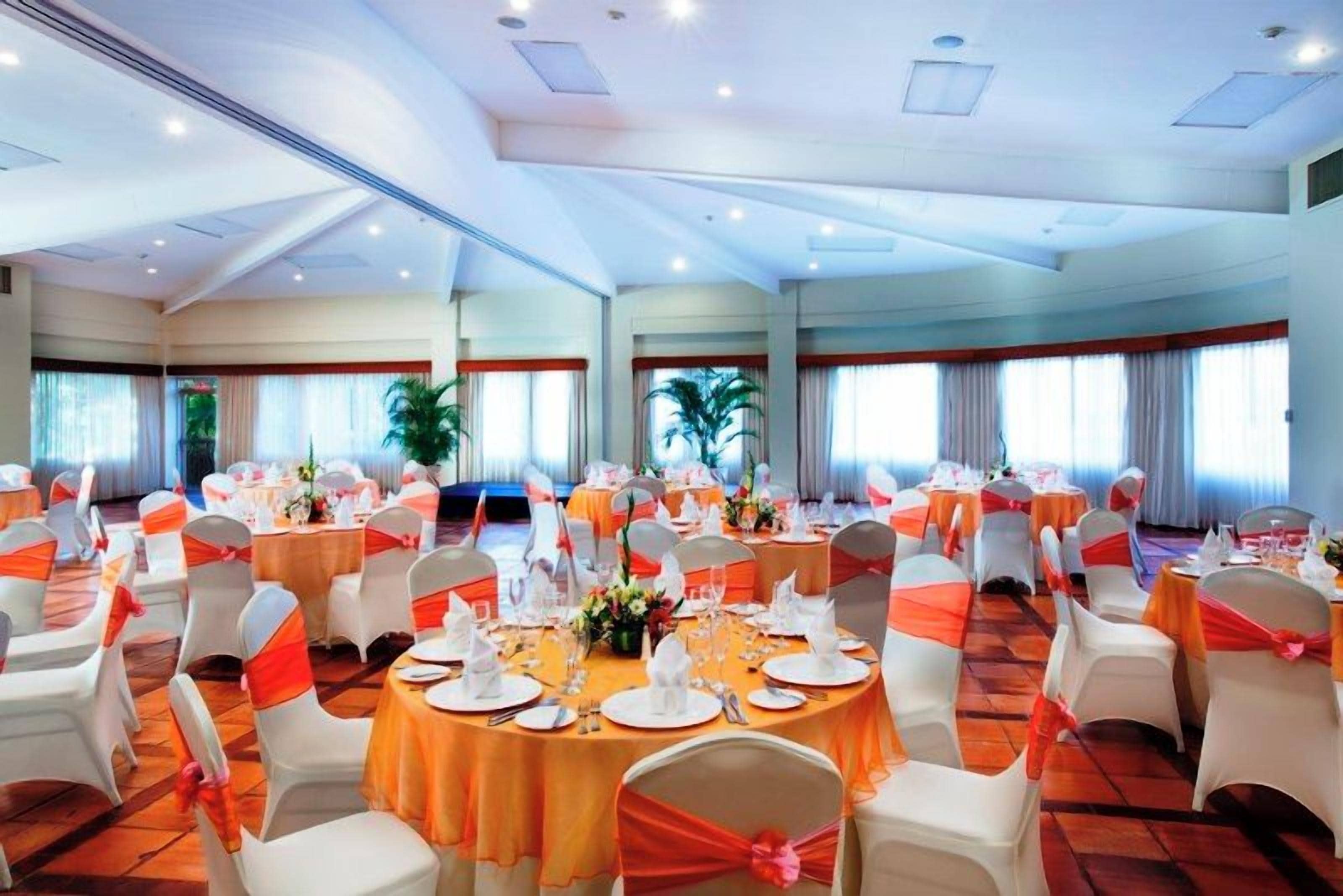 A banquet hall with round tables, white chairs, and orange sashes.
