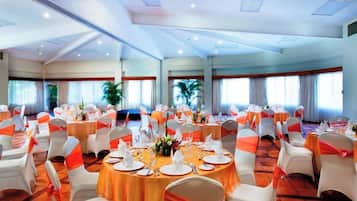 A banquet hall with round tables, white chairs, and orange sashes.