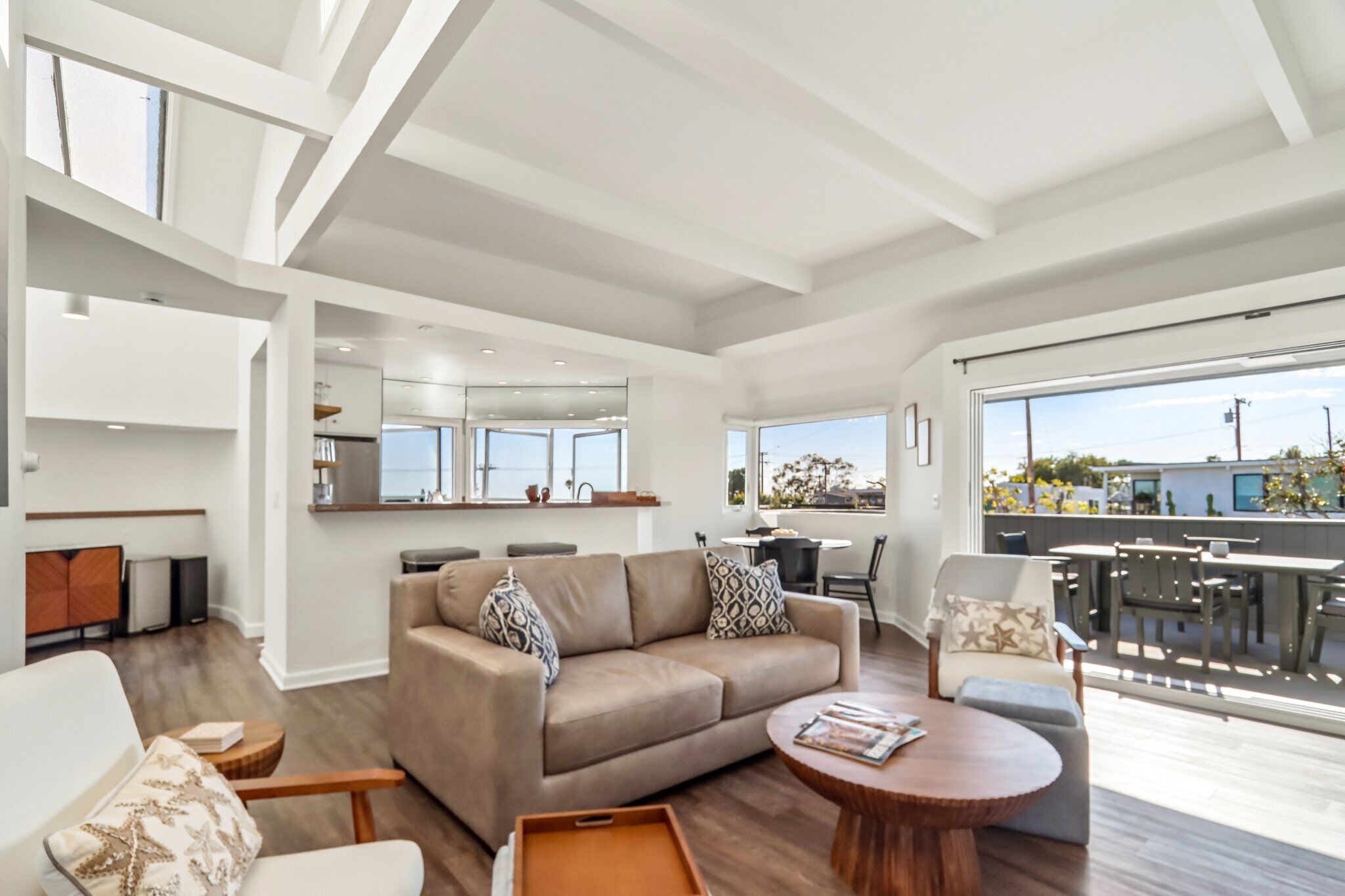 A spacious living area with a sofa, coffee table, and chairs. There is a kitchen area with a window and a dining area with a table and chairs.