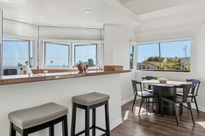 A modern kitchen with a large window, a dining area with a round table and chairs, and a bar stool. - Stunning Ocean-View Home in the Heart of Laguna Beach! Walk to Beach! (Laguna Beach)