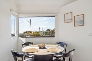 Een eethoek met een ronde tafel, vier stoelen en een schaal koekjes. Er is een raam met uitzicht op gebouwen en bomen.
