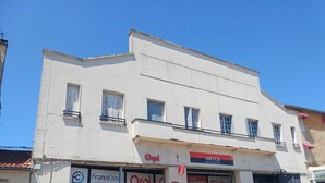 Un edifici blanc amb diverses botigues, incloent cartells visibles d'"Orpi" i "Artus".