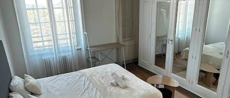 A bedroom with a single bed, a wooden floor, and a large window.