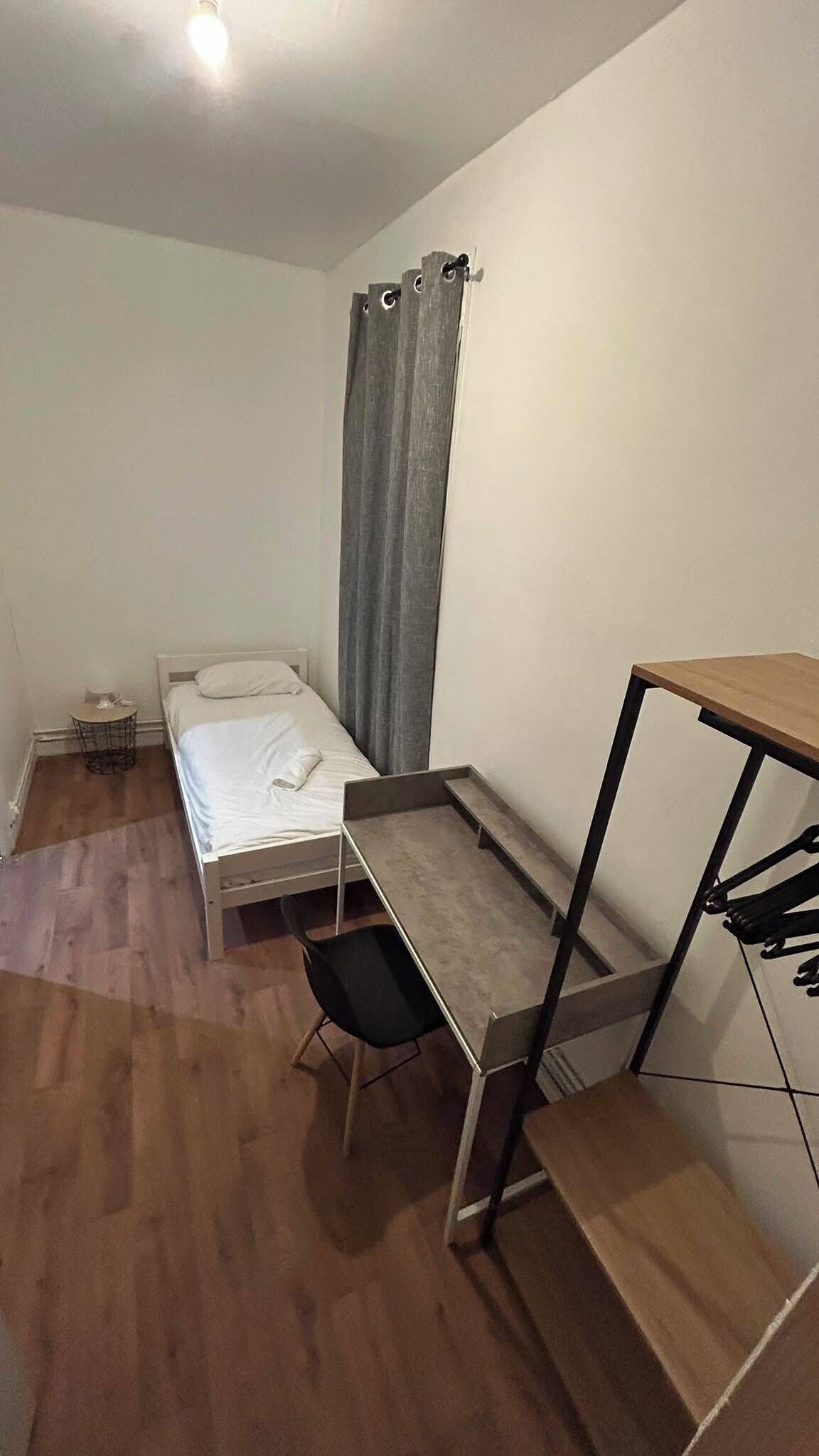 Una stanza piccola e modesta, arredata con un letto, una scrivania e una sedia.