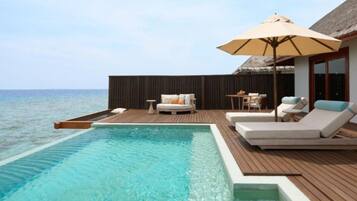 An infinity pool with a wooden deck, lounge chairs, and a table with a canopy.