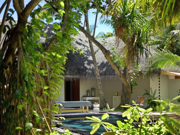A pool area with a thatched-roof structure, a bench, and a chair.