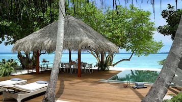 Una terraza de madera con sillones de descanso, una estructura de techo de paja y una piscina infinita con vista al océano.