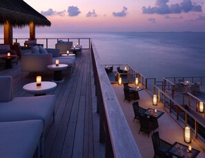 A wooden deck with seating and tables, overlooking the sea.