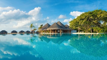 An infinity pool with overwater bungalows and a clear blue sky.