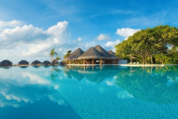 An infinity pool with overwater bungalows and a clear blue sky.