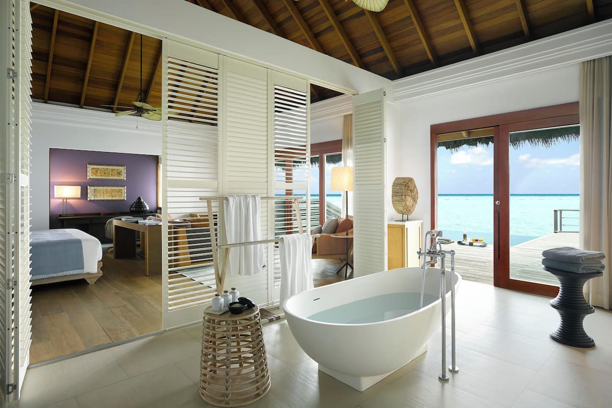 A room with a bathtub, wooden flooring, a ceiling fan, and a view of the ocean.