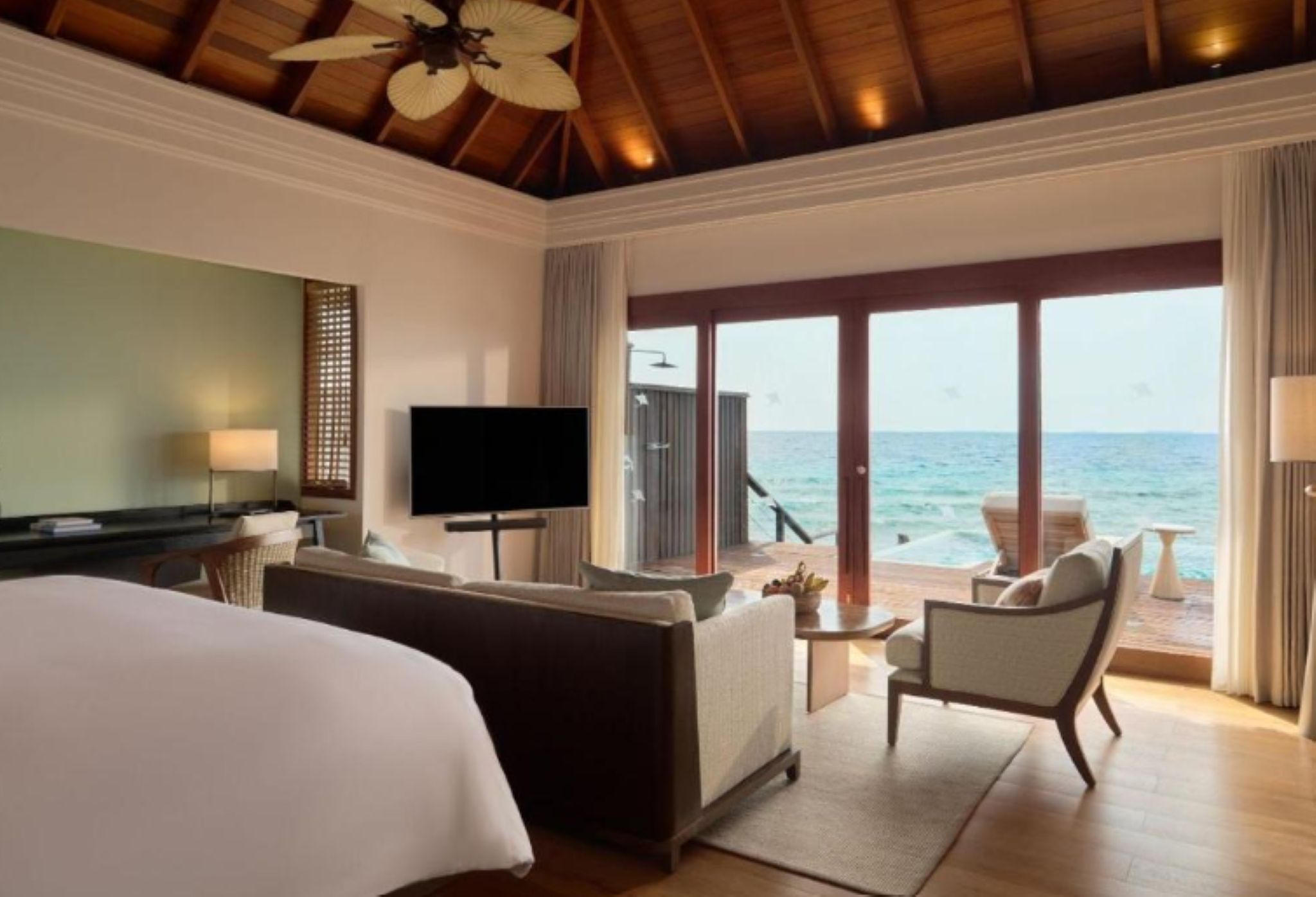 Une chambre d’hôtel avec un lit, une télévision, un canapé, un fauteuil et une vue sur l’océan.