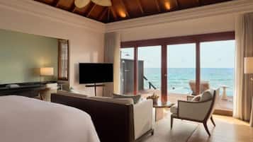 A hotel room with a bed, a TV, a sofa, a chair, and a view of the ocean.