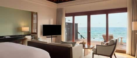 A hotel room with a bed, a TV, a sofa, a chair, and a view of the ocean.
