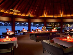 Un restaurante con mesas dispuestas para comer, un ventilador de techo y vistas a un cuerpo de agua.