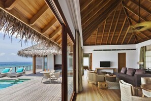 A modern interior with a wooden deck, a pool, and a living area with a TV. - Dusit Thani Maldives (Mudhdhoo)