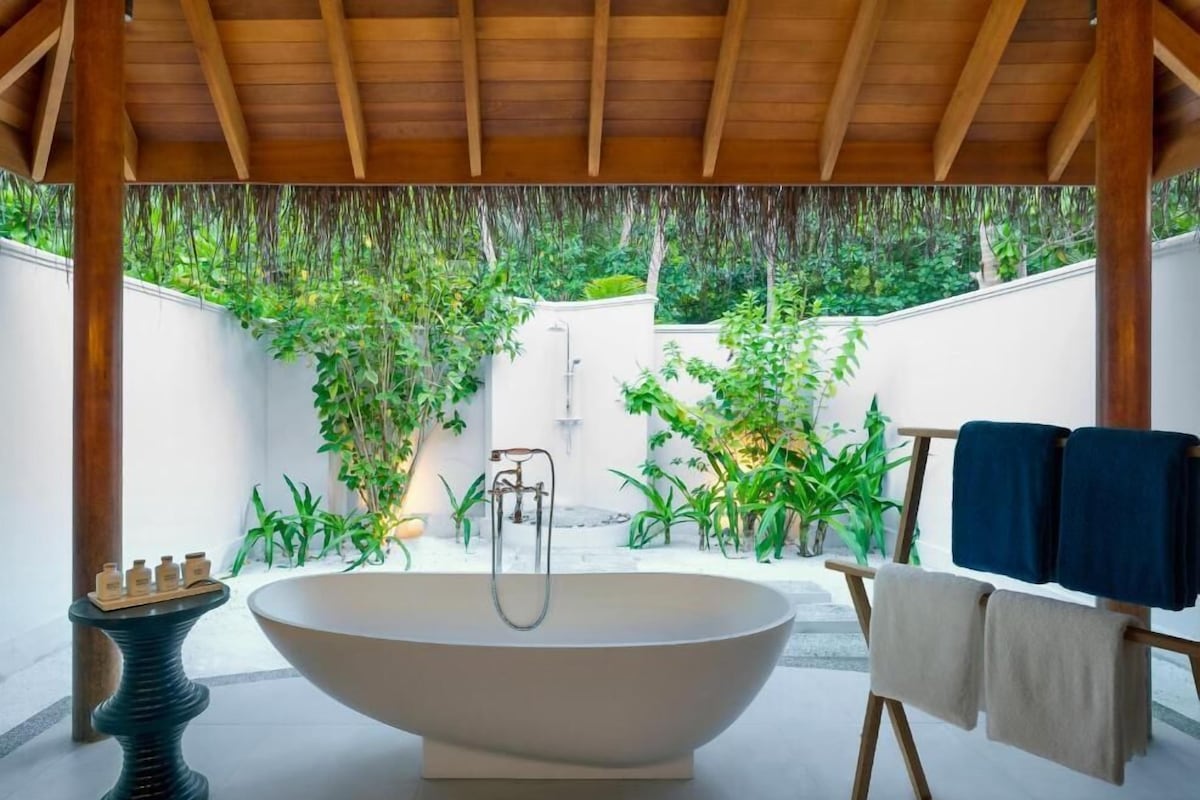 Un baño moderno con una bañera independiente, un banco de madera y un perchero para toallas.