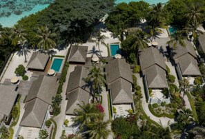 An aerial view of a resort with multiple bungalow-style buildings, each with a pool and surrounded by lush greenery.