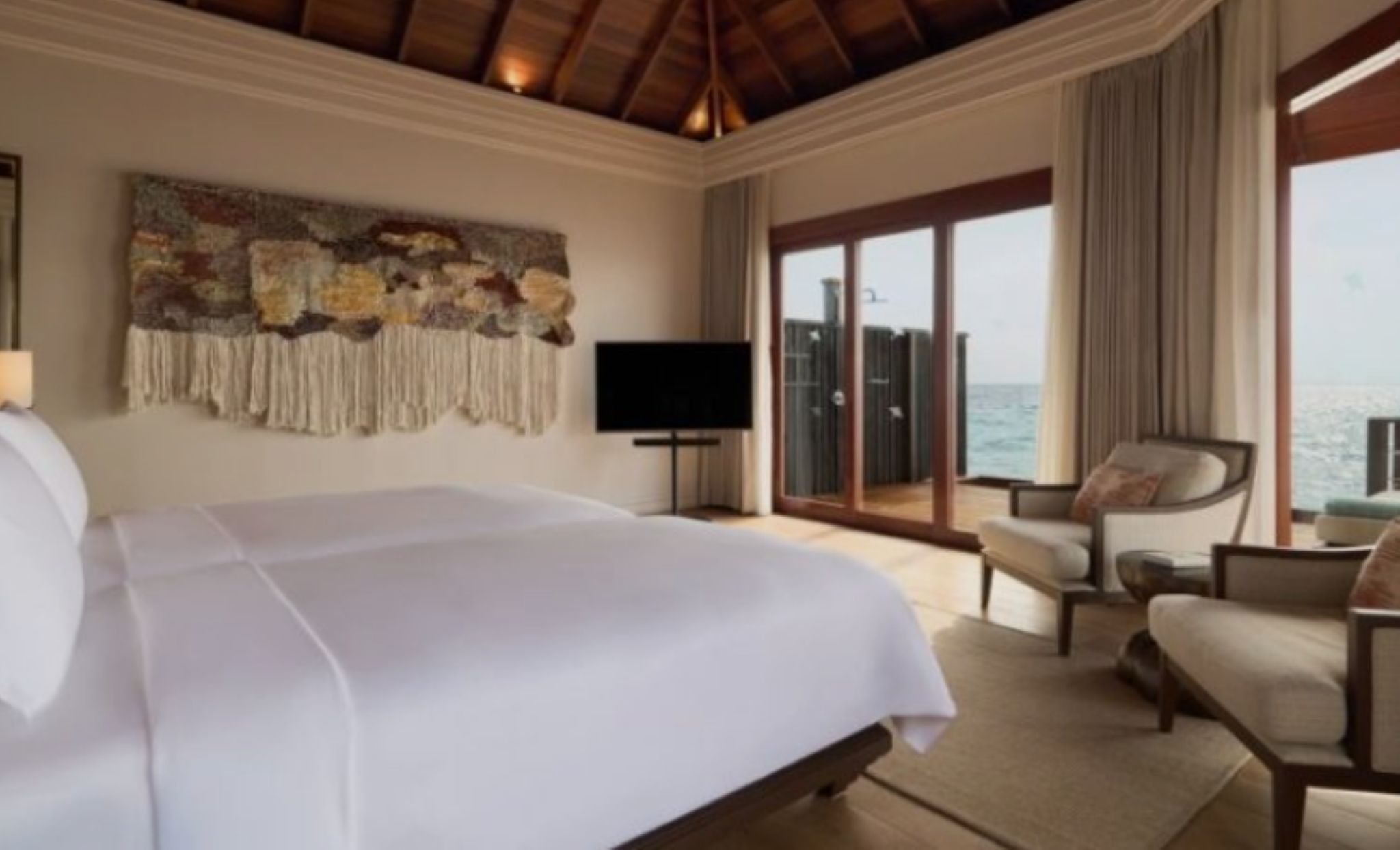 A hotel room with a large bed, a television, a seating area with a view of the sea, and a balcony.