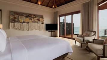 A hotel room with a large bed, a television, a seating area with a view of the sea, and a balcony.