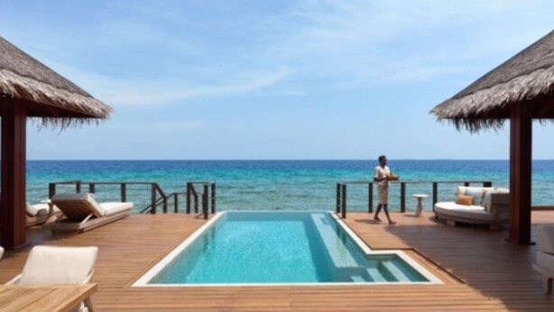 A poolside area with lounge chairs, a pool, and a view of the ocean.