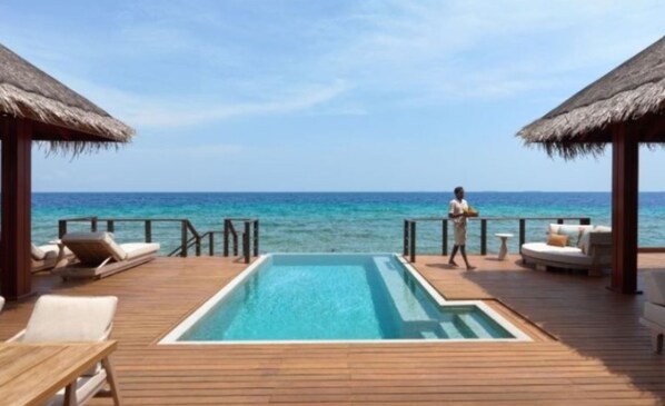 A poolside area with lounge chairs, a pool, and a view of the ocean.