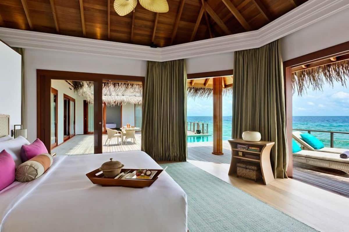 A large bed with a tray of food, a view of the ocean, and a balcony with a table and chairs.