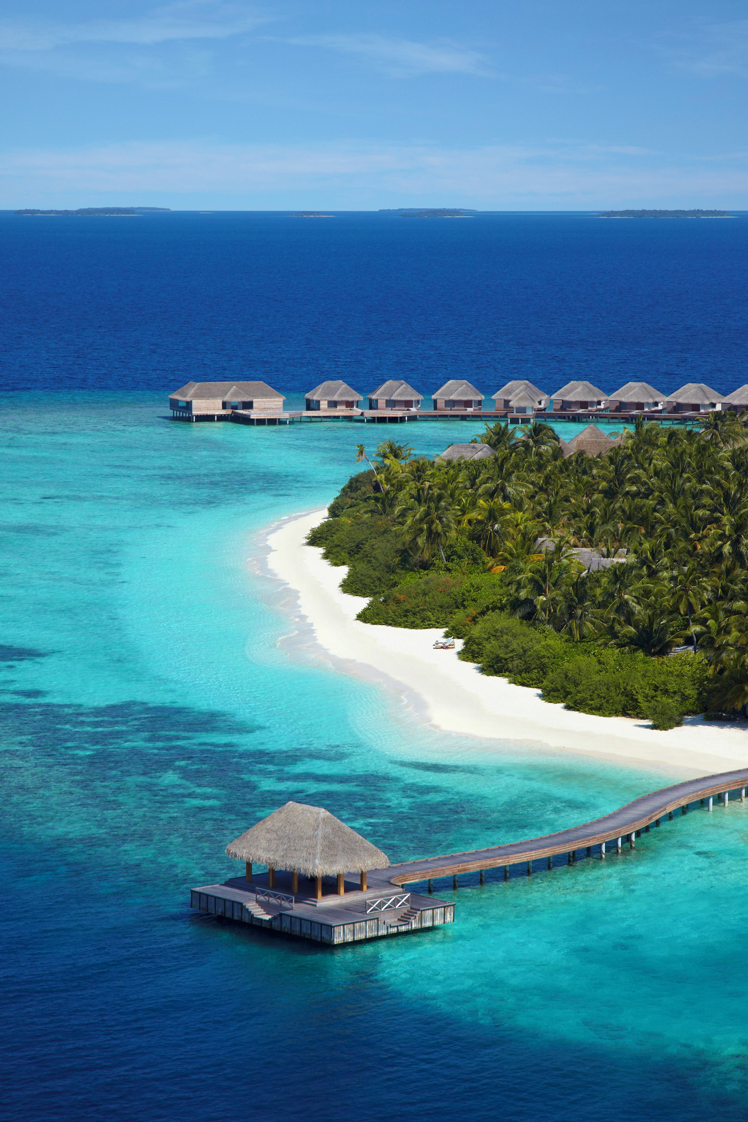An aerial view of a tropical resort with overwater bungalows, a beach, and a pier.