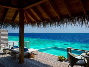 Una terraza de madera con techo de paja, con vista a un mar azul cristalino y una pequeña piscina infinita.