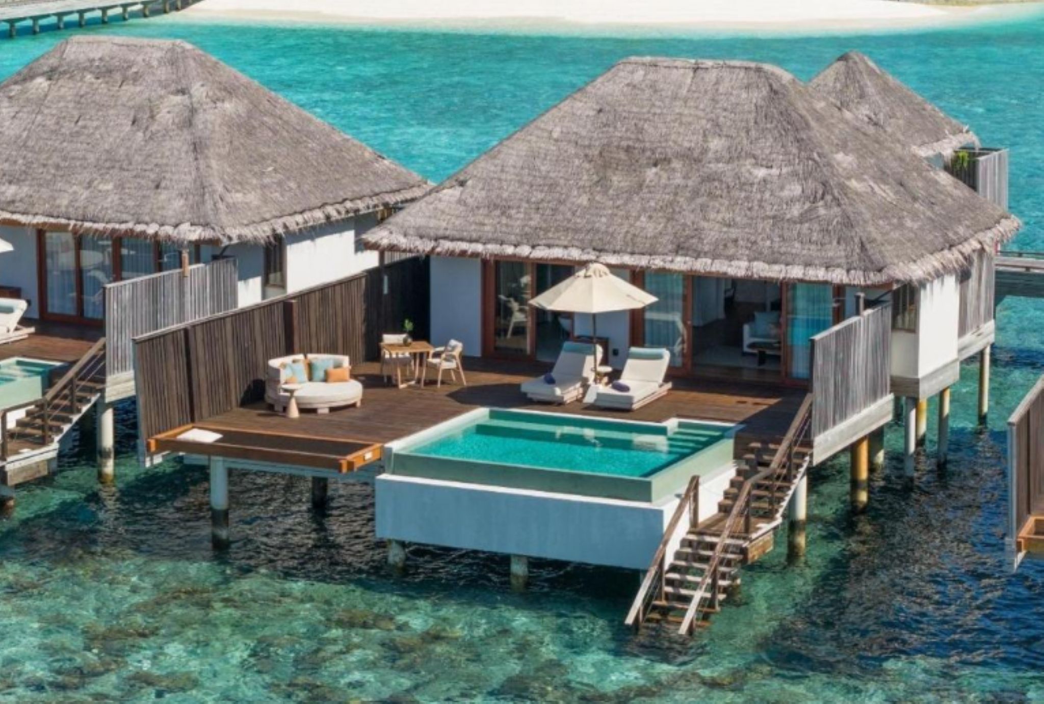 Overwater bungalows with thatched roofs, a pool, and lounge chairs.