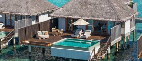 Overwater bungalows with thatched roofs, a pool, and lounge chairs.